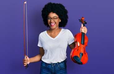 Young african american woman playing violin winking looking at the camera with sexy expression,...