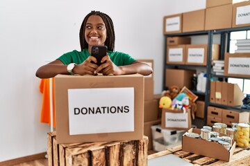 Young african american woman wearing volunteer uniform using smartphone at charity center