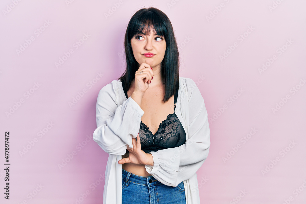 Poster Young hispanic woman wearing lingerie with hand on chin thinking about question, pensive expression. smiling with thoughtful face. doubt concept.