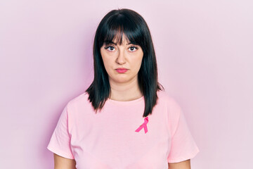 Fototapeta premium Young hispanic woman wearing pink cancer ribbon on shirt thinking attitude and sober expression looking self confident