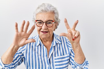 Senior woman with grey hair standing over white background showing and pointing up with fingers number eight while smiling confident and happy.