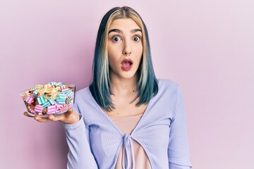 Young modern girl holding bowl of sugar candy scared and amazed with open mouth for surprise, disbelief face