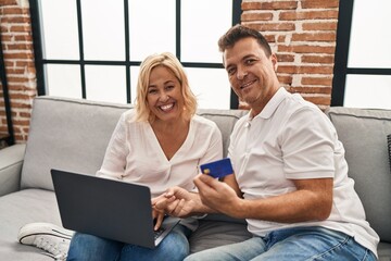 Middle age man and woman using laptop and credit card sitting on sofa at home