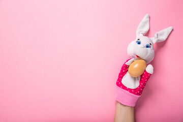 Banner with white bunny and egg in hands on pink background with copy space, empty text place. Christian holiday card Happy Easter. Online toy theater course. Hand puppet. Traditional childhood play.