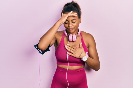 Young african american girl wearing gym clothes and using headphones touching forehead for illness and fever, flu and cold, virus sick
