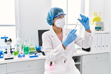 Young latin woman wearing scientist uniform holding vaccine at laboratory