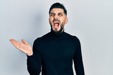 Handsome man with beard presenting with open palm angry and mad screaming frustrated and furious, shouting with anger looking up.