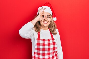 Middle age caucasian woman wearing cook apron and christmas hat smiling happy doing ok sign with...