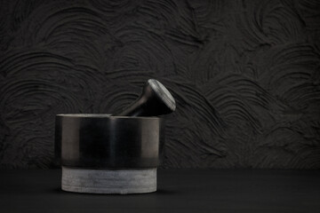 Dark stone mortar with pestle on black background. Space for text.