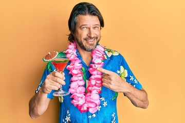 Middle age handsome man wearing hawaiian lei drinking cocktail smiling happy pointing with hand and...