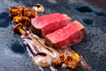 Modern style traditional fried dry aged angus beef tenderloin steak natural with chanterelle mousse parfait and wild cherry relish cream served as close-up on a Nordic design plate