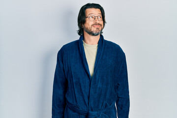 Obraz premium Middle age caucasian man wearing bathrobe and glasses smiling looking to the side and staring away thinking.