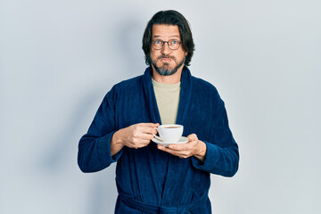 Middle age caucasian man wearing robe drinking coffee puffing cheeks with funny face. mouth...