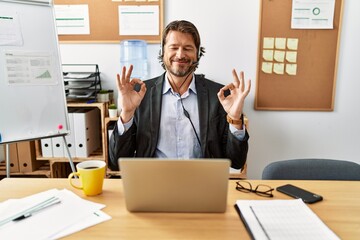 Handsome middle age man wearing call center agent headset at the office relax and smiling with eyes closed doing meditation gesture with fingers. yoga concept. - obrazy, fototapety, plakaty