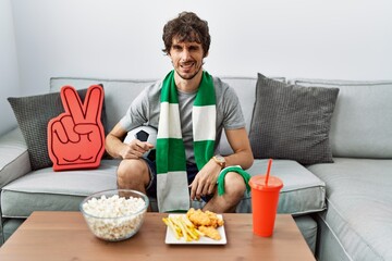 Young hispanic man football hooligan cheering game at home winking looking at the camera with sexy...