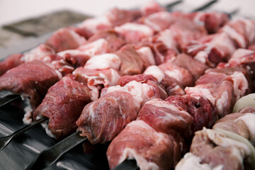Marinated meat, food cooking on skewers on fire. Preparing pork shashlik on a charcoal mangal. Beef grill. BBQ. Side view. Outdoors picnic. Traditional tasty shish. Juicy meal. Close-up.