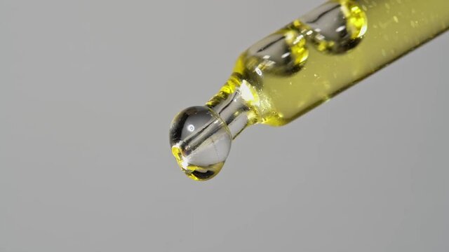 Drops of oil extract dripped from a glass pipette for chemical reactions and aromatherapy. Close up macro.
