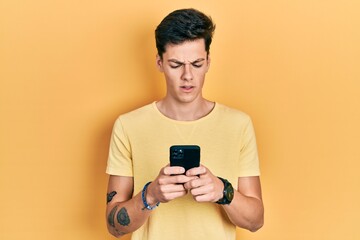 Young hispanic man using smartphone typing message in shock face, looking skeptical and sarcastic,...