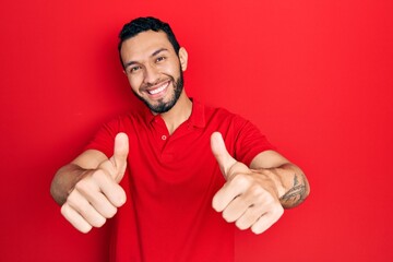 Hispanic man with beard wearing casual red t shirt approving doing positive gesture with hand,...
