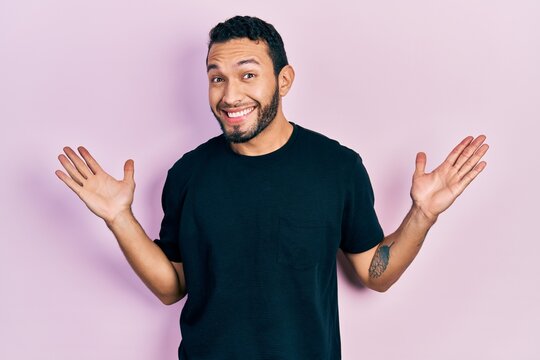 Hispanic man with beard wearing casual black t shirt clueless and confused with open arms, no idea and doubtful face.