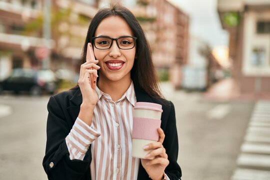 Young hispanic businesswoman talking on the smartphone and drinking coffee at the city.