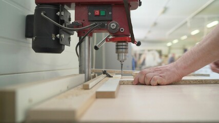 Close-up of a carpenter's hand drilling wood while working in carpentry. A furniture production worker works at a drilling table.