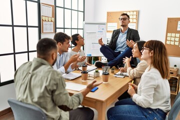 Businessman enjoys meditating during meeting. Sitting on desk near arguing partners at the office.