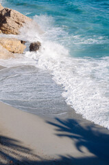 Aerial top view of sea waves hitting rocks on the beach with turquoise sea water. 