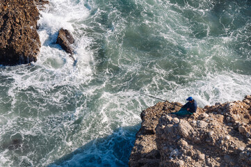 A man with a fishing rod is fishing on the rocks near the sea. Active recreation in nature.