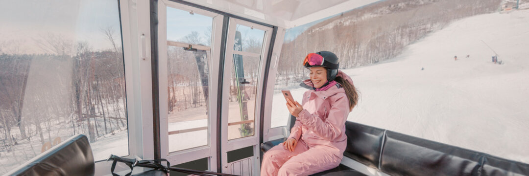 Ski Winter Holidays - skier using phone app in gondola ski lift. Woman smiling looking at mobile smartphone wearing ski clothing, helmet and goggles. Ski winter activity concept panoramic banner
