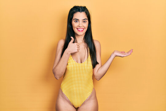 Young hispanic girl wearing swimsuit showing palm hand and doing ok gesture with thumbs up, smiling happy and cheerful