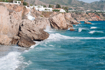 Aerial top view of sea waves hitting rocks on the beach with turquoise sea water. 