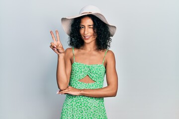 Young latin girl wearing summer hat smiling with happy face winking at the camera doing victory...