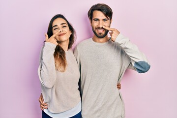Naklejka premium Young hispanic couple wearing casual clothes pointing with hand finger to face and nose, smiling cheerful. beauty concept
