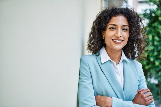 Young hispanic business woman wearing professional look smiling confident at the city leaning on the wall