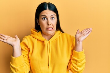 Beautiful brunette woman wearing casual sweatshirt clueless and confused with open arms, no idea and doubtful face.