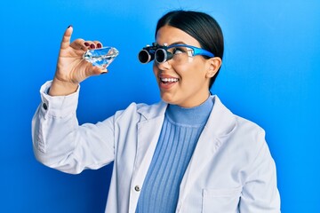 Beautiful brunette jeweller woman holding brilliant diamond stone wearing magnifier glasses smiling looking to the side and staring away thinking.