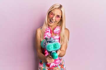 Young blonde woman wearing swimsuit and hawaiian lei using water gun winking looking at the camera...