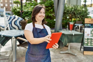 Young down syndrome woman wearing apron using touchpad at coffee shop terrace