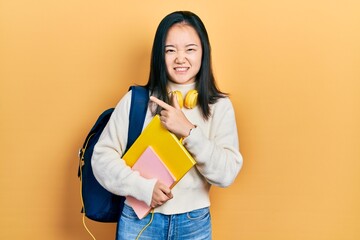 Young chinese girl holding student backpack and books pointing aside worried and nervous with forefinger, concerned and surprised expression