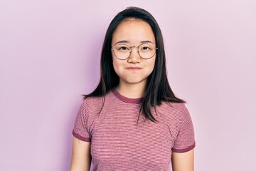 Young chinese girl wearing casual clothes and glasses puffing cheeks with funny face. mouth...