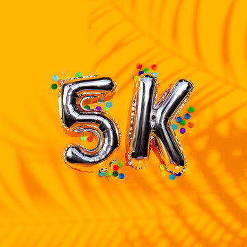 Fotografía para post de Instagram. Para celebrar que se obtuvieron cinco mil seguidores nuevos. Globos metálicos en fondo anaranjado sólido.