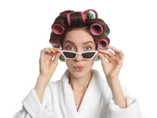 Emotional young woman in bathrobe with hair curlers and sunglasses on white background