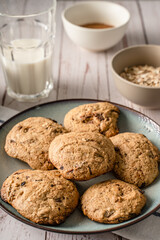 Close up front view on crunchy oatmeal chip cookies fresh baked biscuits with chocolate and cocoa in a plate on the table and ingredients beside homemade food concept