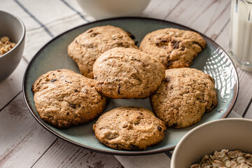 Close up front view on crunchy oatmeal chip cookies fresh baked biscuits with chocolate and cocoa in a plate on the table and ingredients beside homemade food concept