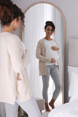 Pregnant young African-American woman near mirror at home