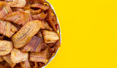 Banana slice chips in bamboo basket on yellow background.