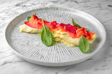 Pancake with Philadelphia cheese with salmon, colored beets in a festive plate on a marble background. Restaurant banquet menu.