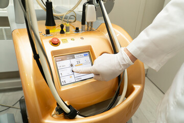 The hand of a beautician in a glove presses the monitor in a modern laser machine .Apparatus for...