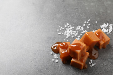 Yummy caramel candies with sauce and sea salt on grey table, space for text